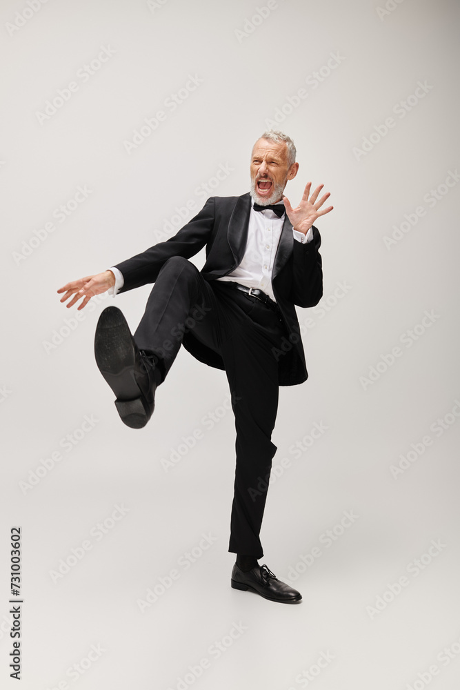 appealing joyous mature man with elegant dapper style with beard dancing happily on gray backdrop