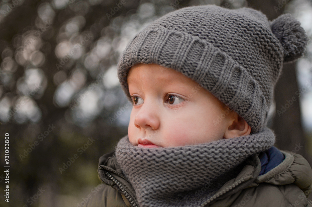 Horizontal portrait of a sad or pensive child in a warm hat and scarf looking to the side on a cold winter's day at dusk. Concept of nostalgia, sadness.. Horizontal portrait of a sad or pensive child in a warm hat and scarf looking to the side on a cold winter's day at dusk. Concept of nostalgia, sadness..