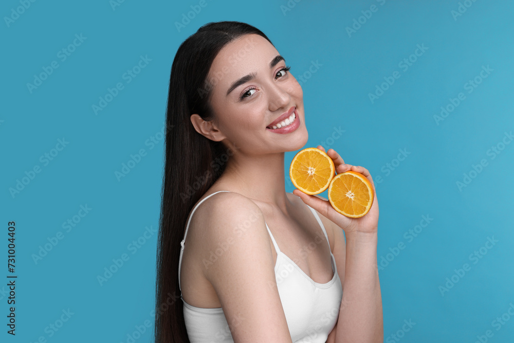 Beautiful young woman with pieces of orange on light blue background Beautiful young woman with pieces of orange on light blue background