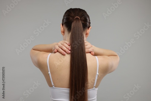 Woman touching her neck on grey background, back view