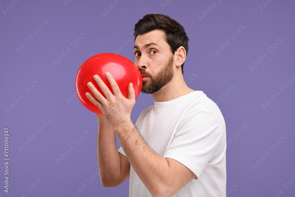 Man inflating red balloon on purple background Man inflating red balloon on purple background