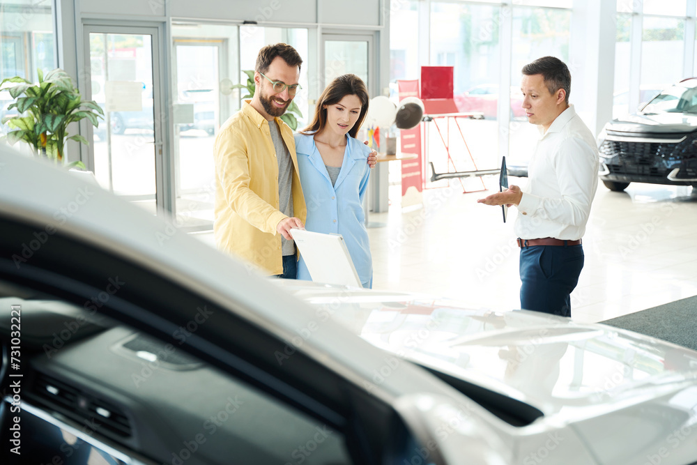 Couple in a car dealership communicates with a consultant Couple in a car dealership communicates with a consultant