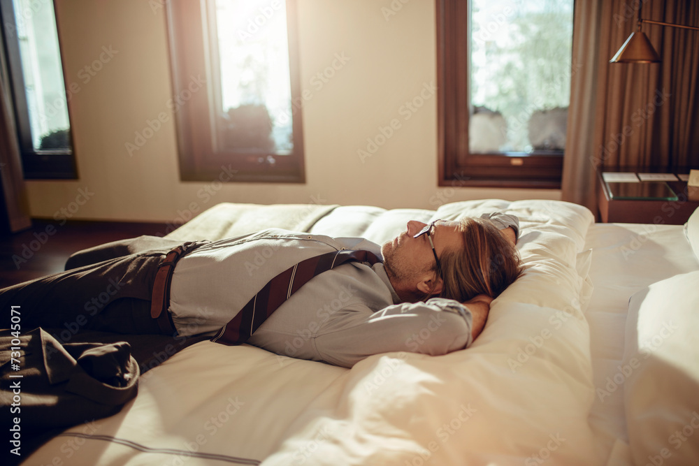 Exhausted businessman taking a nap on hotel bed with clothes on Exhausted businessman taking a nap on hotel bed with clothes on