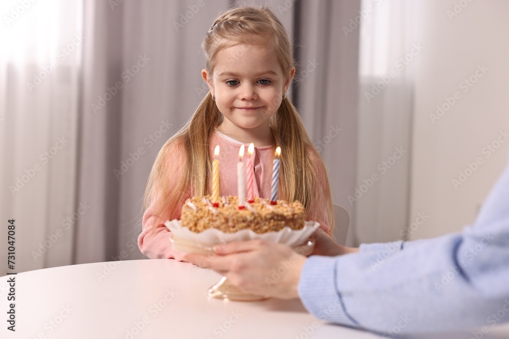 Birthday celebration. Mother holding tasty cake with burning candles near her daughter indoors Birthday celebration. Mother holding tasty cake with burning candles near her daughter indoors