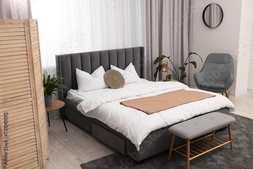 Stylish bedroom interior with large bed, ottoman, lamp and houseplants