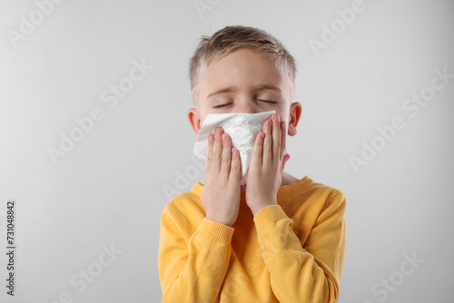 Sick boy with tissue coughing on gray background. Cold symptoms