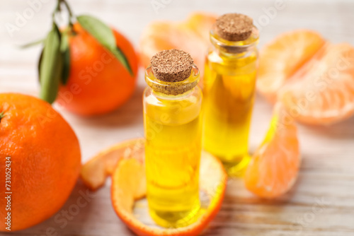 Bottles of tangerine essential oil, fresh fruits and peel on white wooden table, closeup