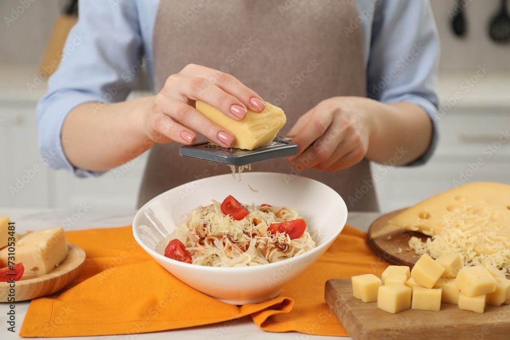 Woman grating cheese onto delicious pasta at white table in kitchen, closeup