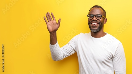 A joyful man waves his hand against a yellow background, with ample space for text, creating a vibrant and cheerful scene. © vadymstock