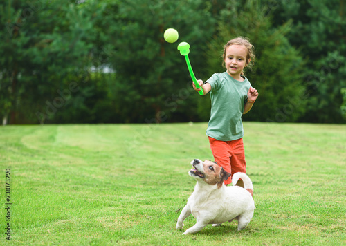 Fun game at backyard with a dog. Girl uses a ball thrower to play fetch with a pet photo