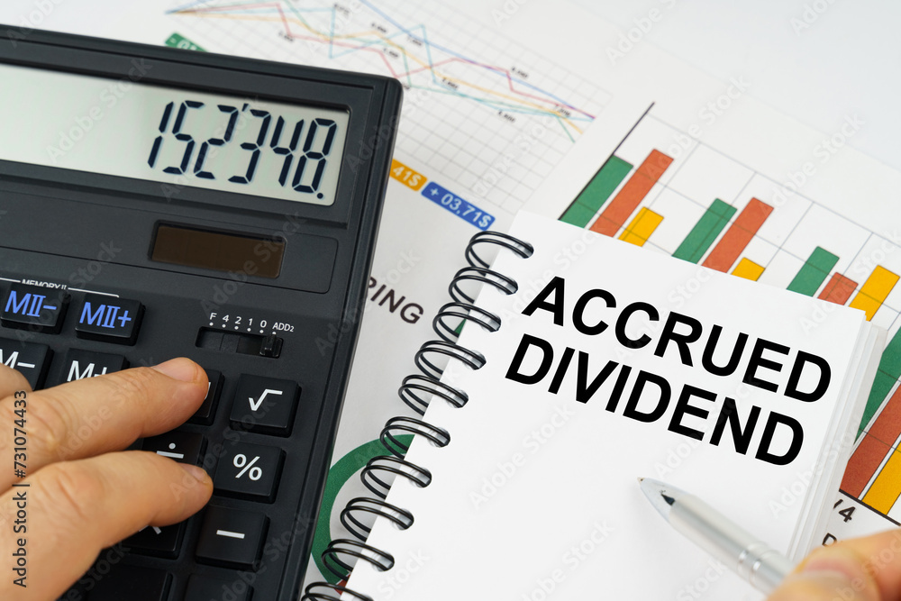 On the table there is a calculator, reports with graphs and a notepad with the inscription - ACCRUED DIVIDEND On the table there is a calculator, reports with graphs and a notepad with the inscription - ACCRUED DIVIDEND