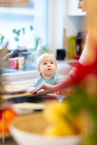Mother and little toddler baby boy making pancakes for breakfast together in domestic kitchen. Family, lifestyle, domestic life, food, healthy eating and people concept