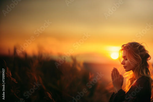 femme caucasienne blonde de profil qui prie dans la nature, au lever du soleil. Copyspace, fond mordoré avec espace négatif pour texte, religion, méditation, bien-être