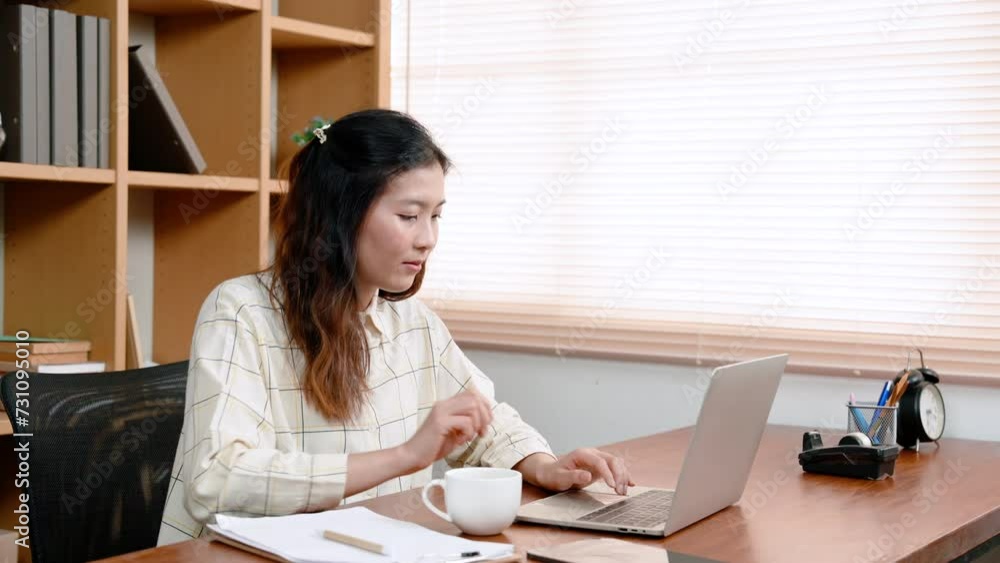 Asian woman holding coffee cup in hand, drinking while working, Putting down his glass, eyes turned intently laptop screen on table, before picking up coffee mug again, comes up smelling coffee. Asian woman holding coffee cup in hand, drinking while working, Putting down his glass, eyes turned intently laptop screen on table, before picking up coffee mug again, comes up smelling coffee.