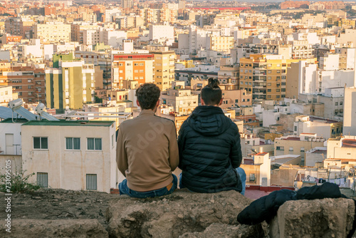 dos chicos jóvenes sentados observando toda la ciudad desde un mirador en la montaña  © Martin