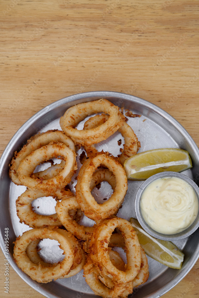 Seafood. Closeup view of fried squid rings with lemon and a dipping sauce in a metal dish on the wooden table. Seafood. Closeup view of fried squid rings with lemon and a dipping sauce in a metal dish on the wooden table.
