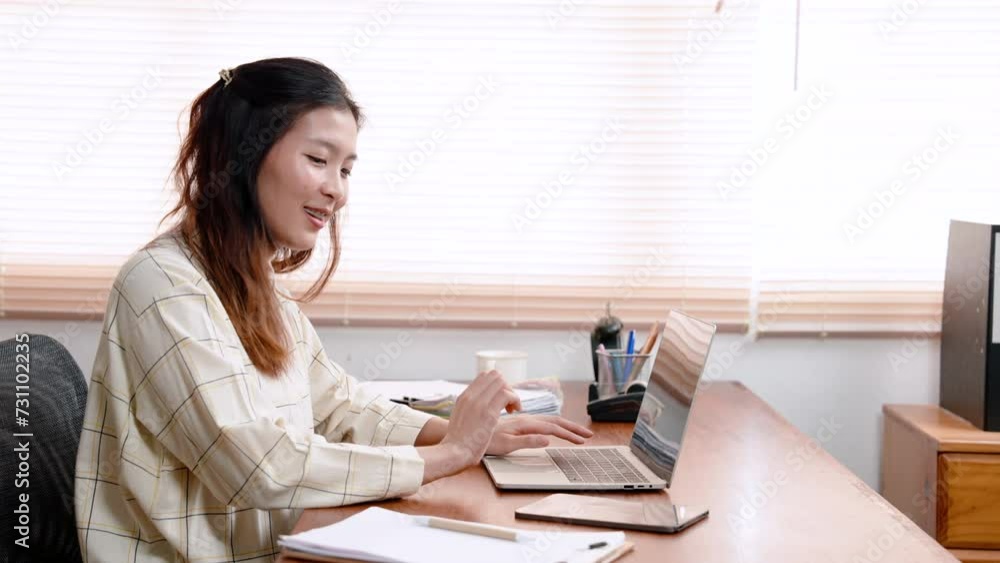 Beautiful Asian office worker, sitting working on laptop computer placed on table in front, with carefree expression, reached out picked up notebook with important things do or write down. Beautiful Asian office worker, sitting working on laptop computer placed on table in front, with carefree expression, reached out picked up notebook with important things do or write down.