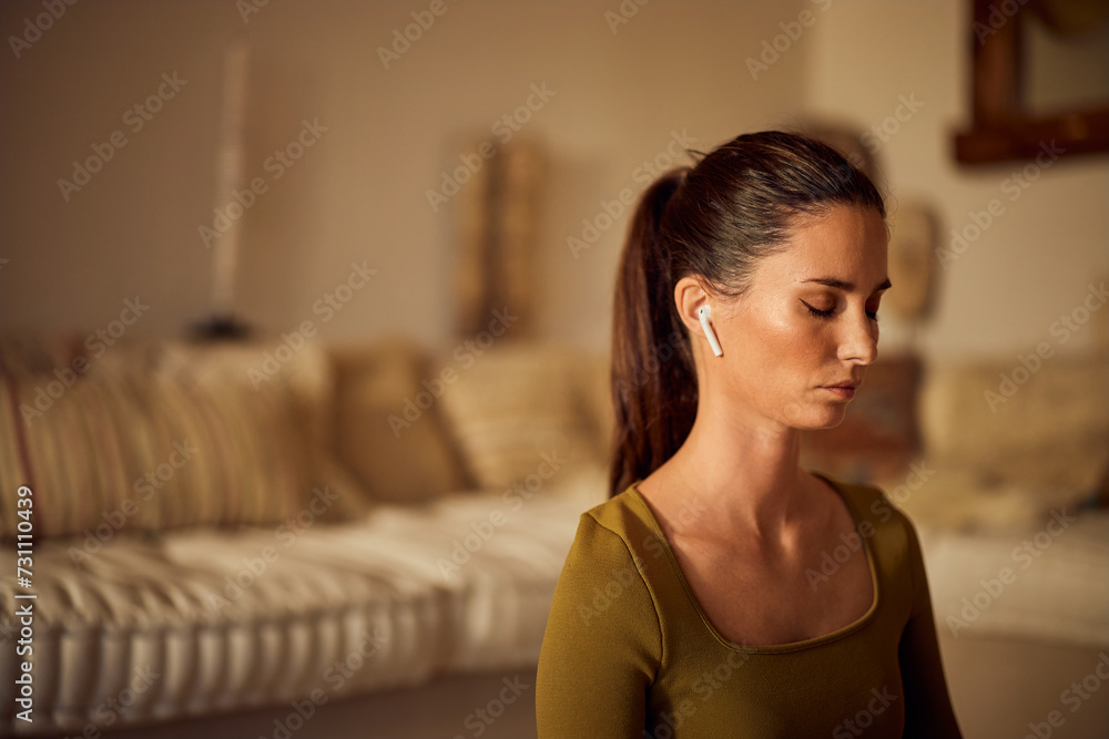 Side profile of a relaxed female, meditating at home, using earphones, and listening to calm music. Side profile of a relaxed female, meditating at home, using earphones, and listening to calm music.