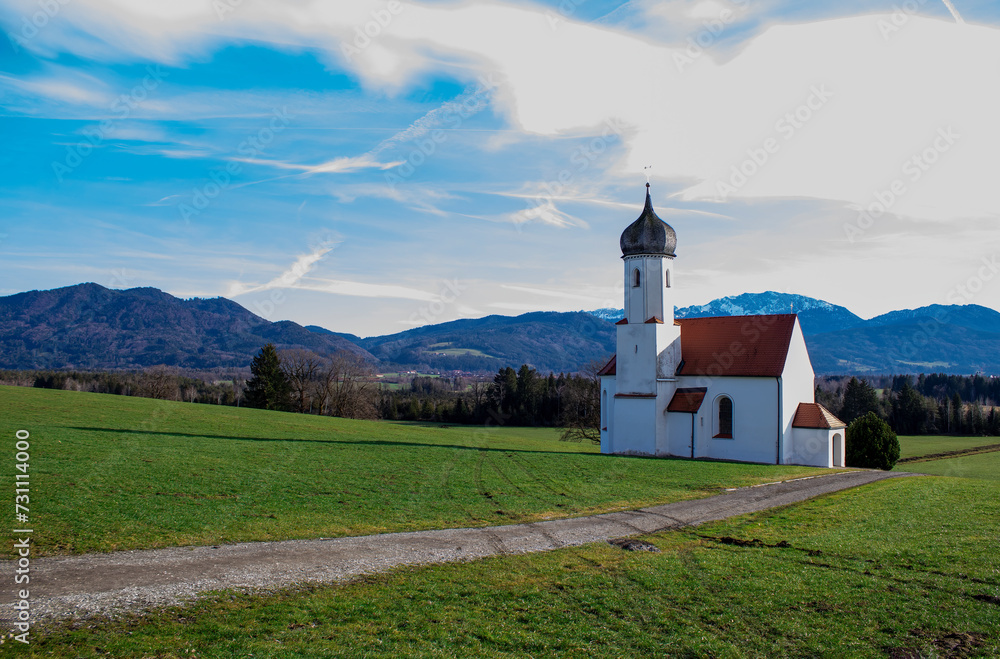 Idyllic landscape, church against the backdrop of the Alps mountains with mountain chalets and green fields
