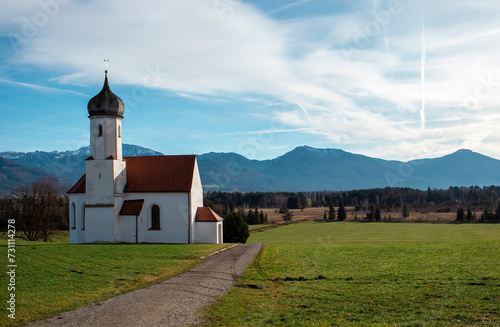 Idyllic landscape, church against the backdrop of the Alps mountains with mountain chalets and green fields