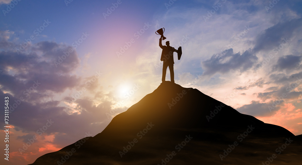 Silhouette victory businessman with trophy climbed to the top of mountain over the sky and sun light background. Success, Achieving goal, Leadership, Career, Winner, and Business achievement Concept.