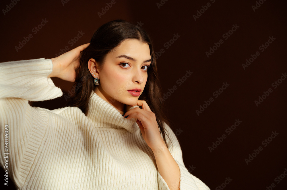 Fashionable confident woman wearing oversized white knitted turtleneck sweater, trendy silver earrings, posing on brown background. Close up studio fashion portrait. Copy, empty blank space for text Fashionable confident woman wearing oversized white knitted turtleneck sweater, trendy silver earrings, posing on brown background. Close up studio fashion portrait. Copy, empty blank space for text