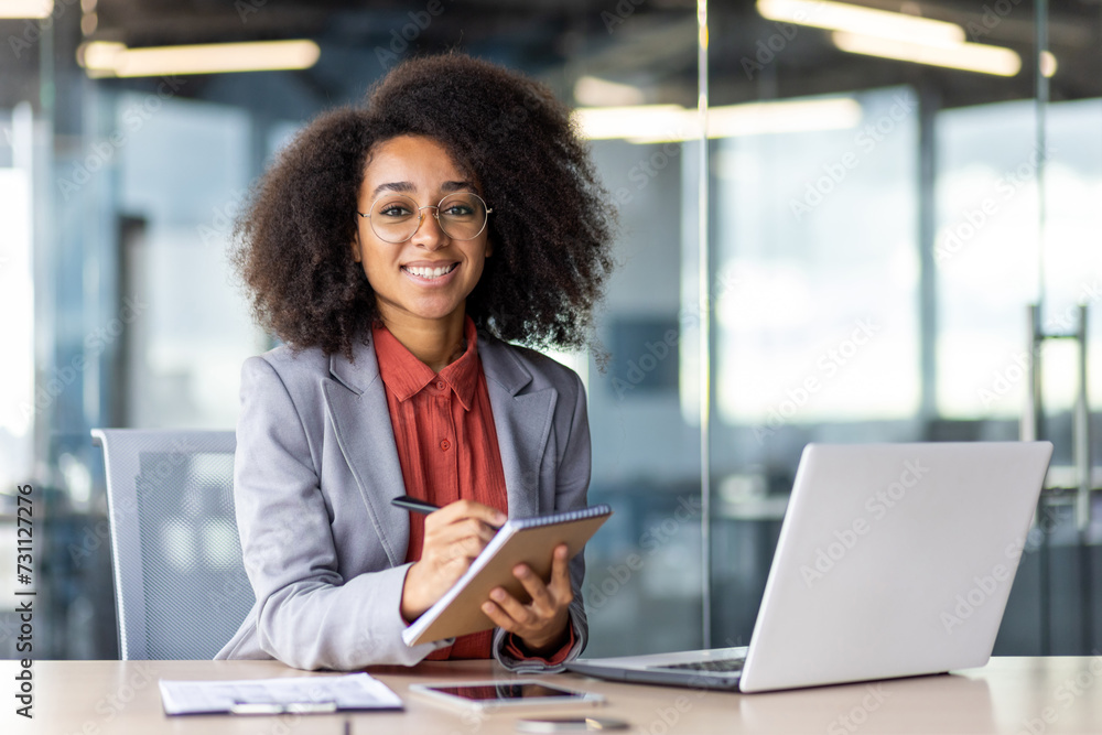 A white-collar worker sits at a desk with a laptop and a tablet, surrounded by furniture. She smiles while working on her personal computer. A white-collar worker sits at a desk with a laptop and a tablet, surrounded by furniture. She smiles while working on her personal computer.