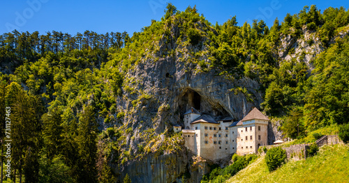 Panorama of Predjama castle built in a cave in Slovenia. Popular tourist attraction and historic monument in an idyllic valley near Postojna Caves on a summer day. Wide angle scenery and major sight. photo