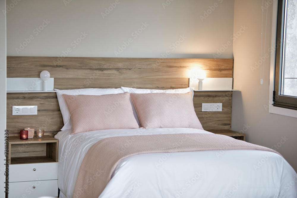 Cozy modern bedroom interior with soft pink pillows, white bedding, and a warm bedside lamp.