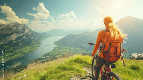 Young athletic woman on top of a mountain with a bicycle and enjoying the view of the stunning valley landscape. © Evgeniia