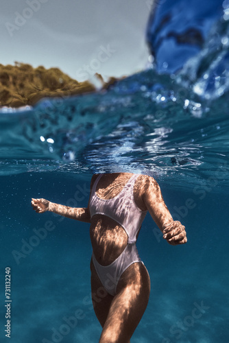 Underwater view of a person in a white swimsuit gliding gracefully with light patterns dancing on the skin