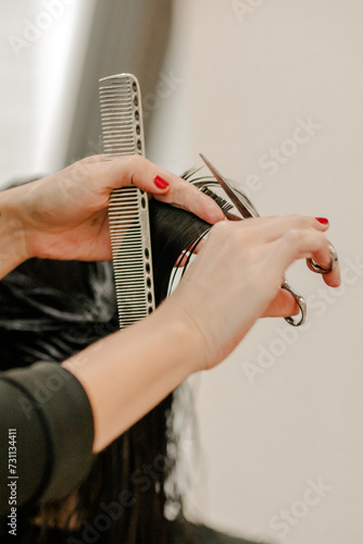 Hairdresser s hands cutting hair with scissors and comb