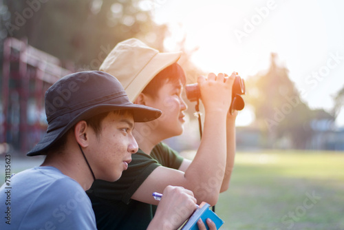 Asian teenboys learning nature by using binoculars to watch birds and insects in public park during summer camp of their school, idea for learning creatures and wildlife animals outside the classroom. photo