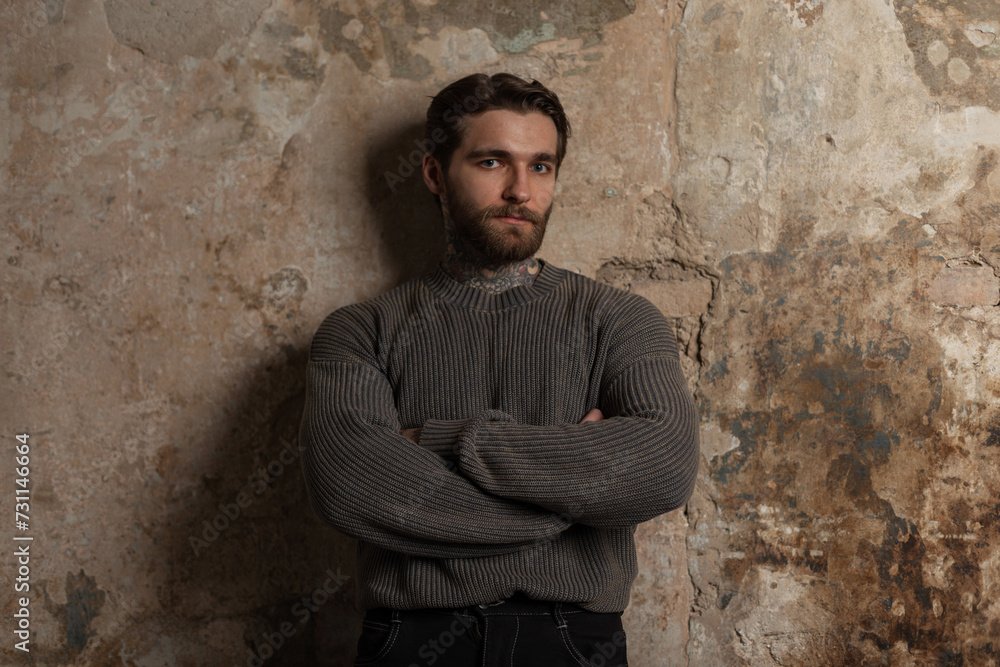 brutal successful handsome hipster man with a hairstyle and beard in a fashion vintage sweater stands near a concrete grunge wall brutal successful handsome hipster man with a hairstyle and beard in a fashion vintage sweater stands near a concrete grunge wall