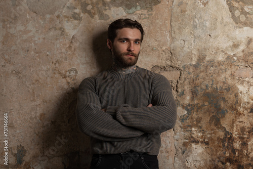 brutal successful handsome hipster man with a hairstyle and beard in a fashion vintage sweater stands near a concrete grunge wall