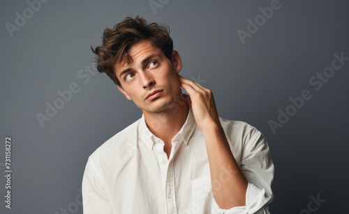 A man wearing a white shirt is holding his hand to his ear, attentively listening.