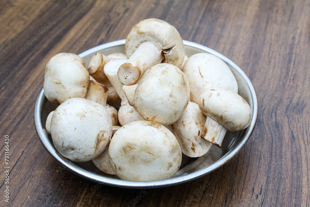White mushrooms in a plate on wooden background 