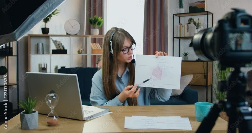 Attractive woman in headphones recording video on camera while explaining results of her research about opportunities of software Attractive woman in headphones recording video on camera while explaining results of her research about opportunities of software