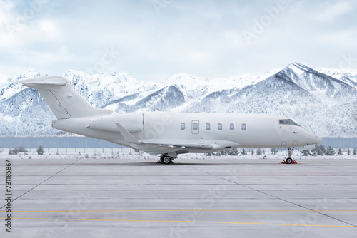 Modern white private jet at the airport apron on the background of high picturesque snow capped mountains