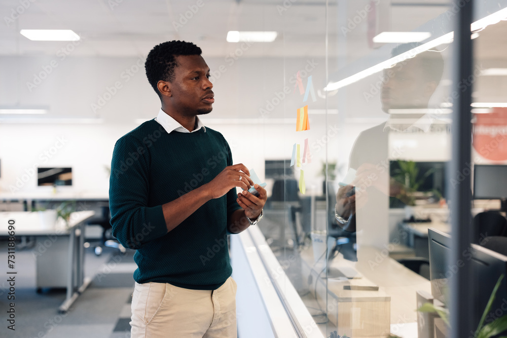 African american man using colorful sticky notes on the glass wall in the office African american man using colorful sticky notes on the glass wall in the office