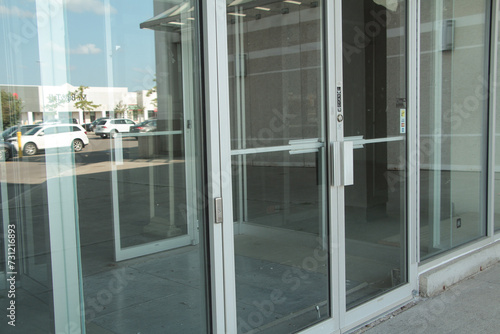 generic glass store doors and windows front entrance with reflection of parking lot and sky