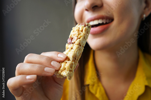 Young woman eating a nuts cereal bar without sugar on gray background