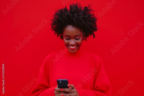 Happy African Woman In Red Sweatshirt Checks Phone Against Red Backdrop