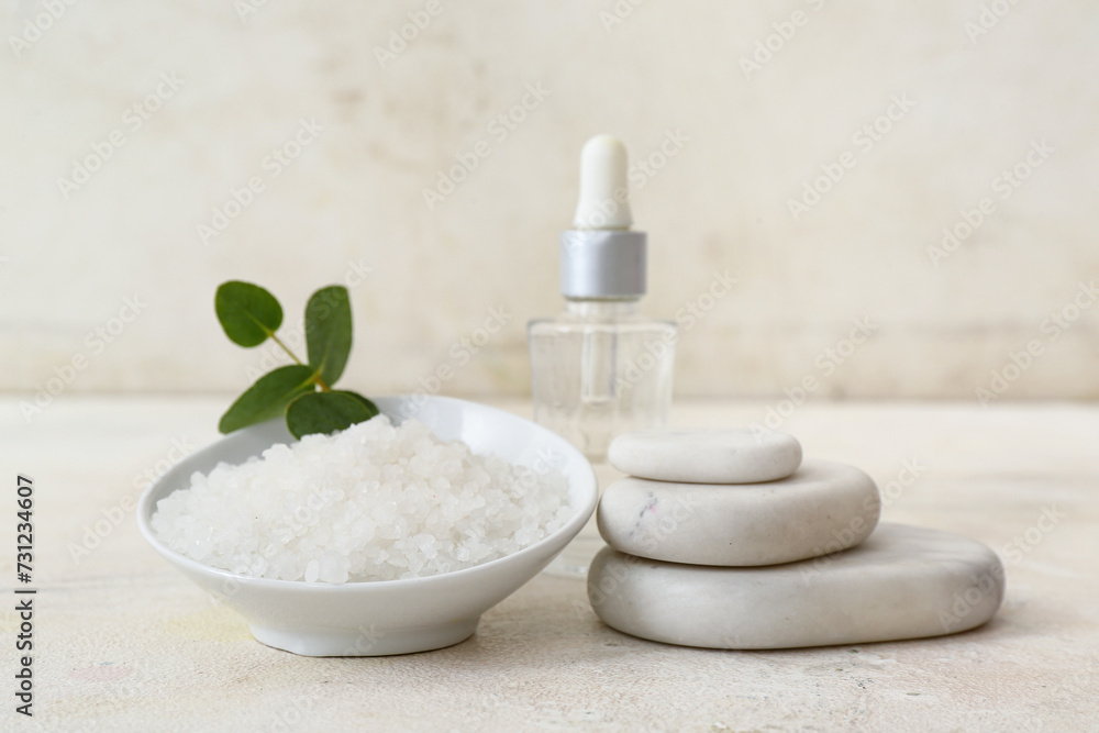 Bowl of sea salt, spa stones and bottle of essential oil on light table Bowl of sea salt, spa stones and bottle of essential oil on light table