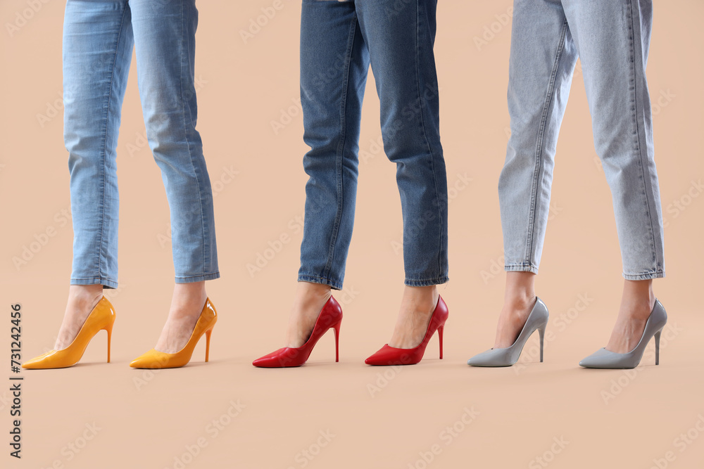 Female legs wearing different high heeled shoes on beige background