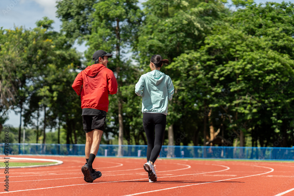 Asian Couple jogging and running outdoors at sport stadium. Happy Man woman wearing sportswear jogging. Male and female in running uniform at outdoor. Workout exercise. Healthy and lifestyle.