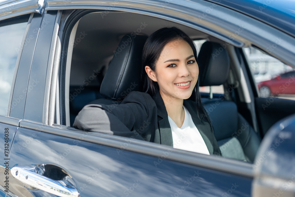 Young beautiful asian business women in suit getting new car. She very happy and excited. Smiling female driving vehicle on the road on a bright day.