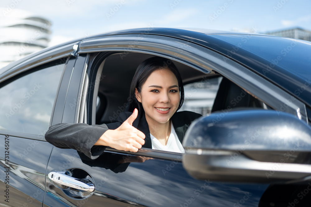Young beautiful asian business women in suit getting new car showing thumbs up. She very happy and excited. Smiling female driving vehicle on the road on a bright day. Young beautiful asian business women in suit getting new car showing thumbs up. She very happy and excited. Smiling female driving vehicle on the road on a bright day.