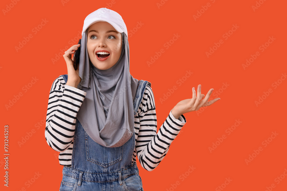Young Muslim woman in hijab talking by mobile phone on orange background Young Muslim woman in hijab talking by mobile phone on orange background