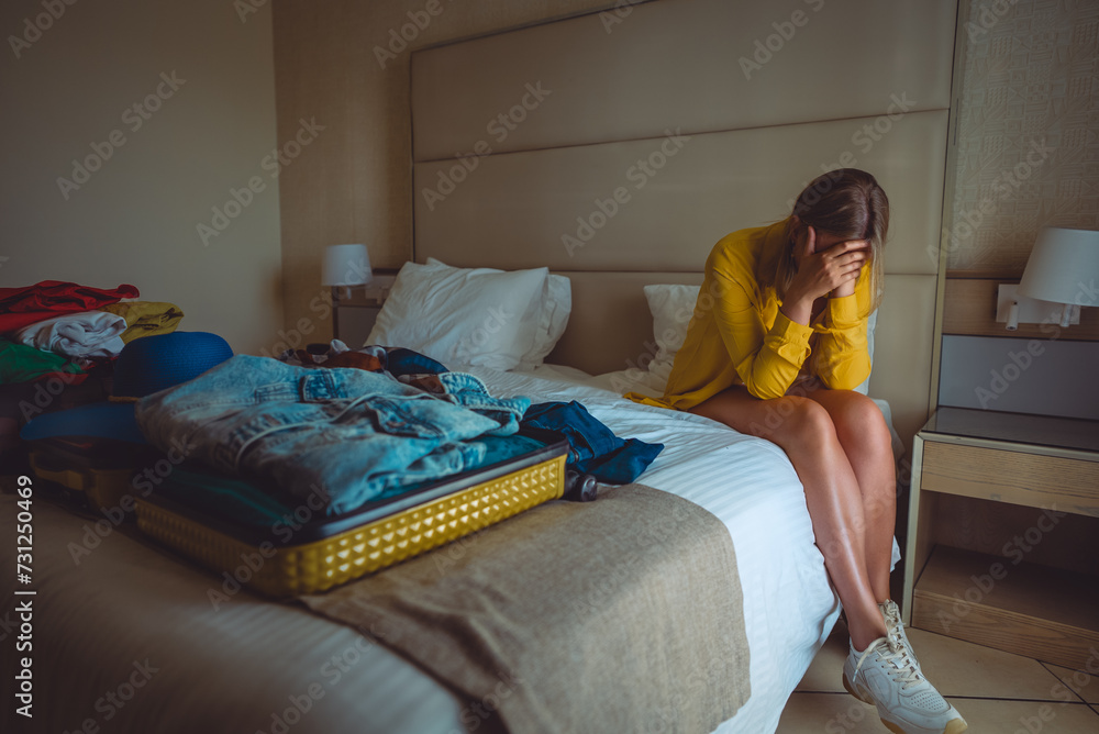 Obraz premium Flight cancellation. Upset woman sitting on bed with suitcases with clothes.